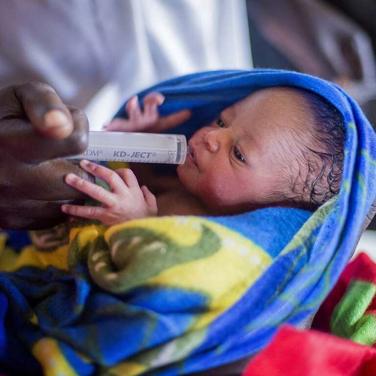 A newborn baby receives medicine from a syringe. 