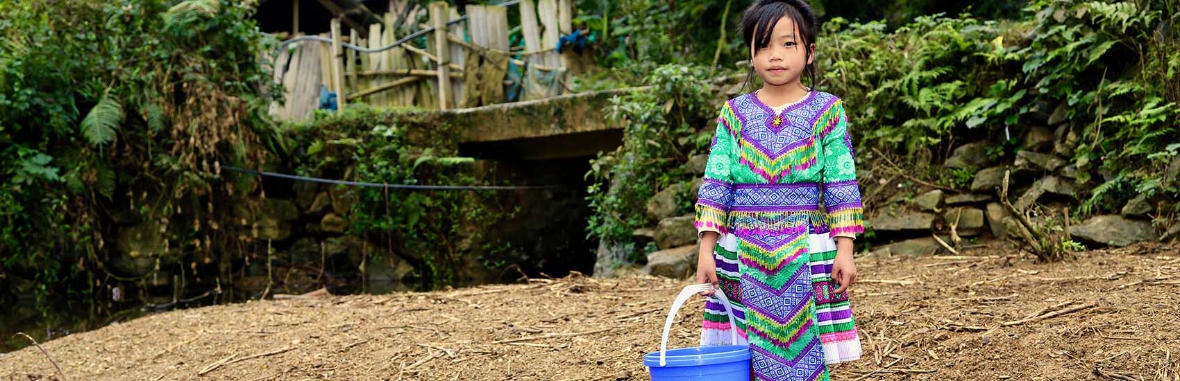 In Vietnam, a girl stands near a river and holds a water bucket. 