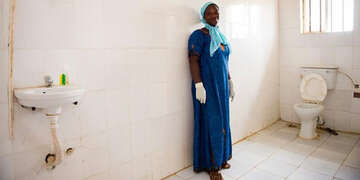 A woman in latex gloves stands in the bathroom of a health care facility.