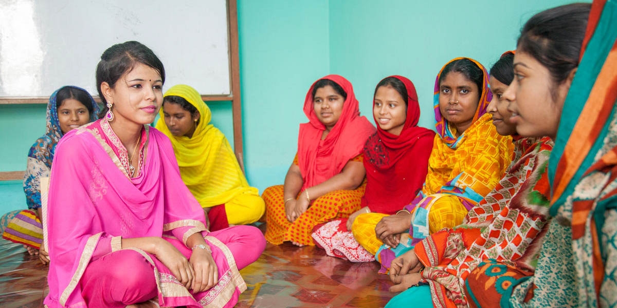 A group of women seated on the floor sit cross-legged and listen intently to one another during a discussion of vocational training of working teenagers in Bangladesh. Save the Children supports programs around the world aimed at changing dangerous working conditions for children. Photo credit: Save the Children, March 2017.