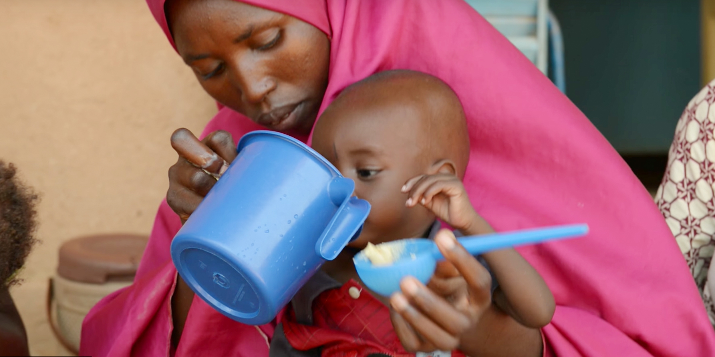 A woman feeds her child from a blue cup.