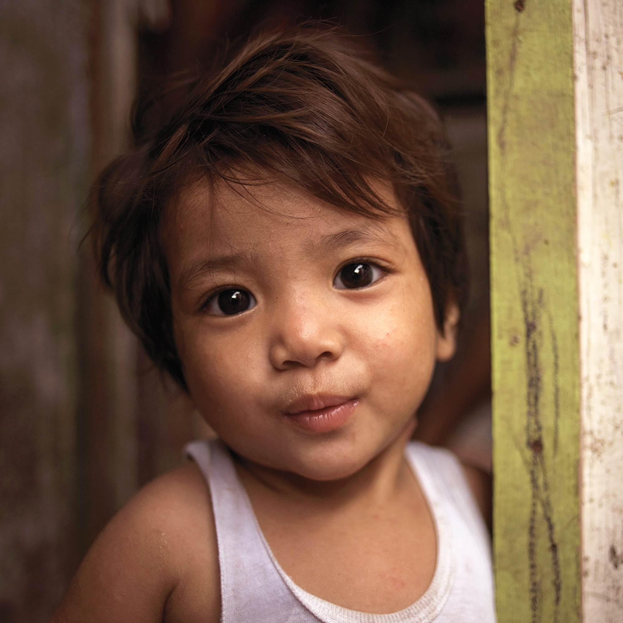 In the Philippines, a young girl smiles while leaning against the frame of a doorway.