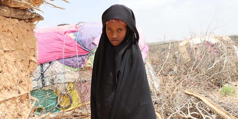 In Somalia, a girl stands in front of a modest hut with clothing hanging out to dry.