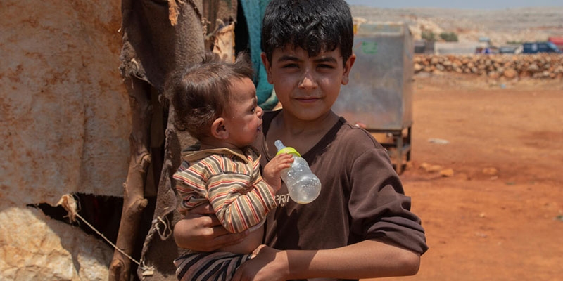 A young boy looks at the camera and is holding his younger brother. 