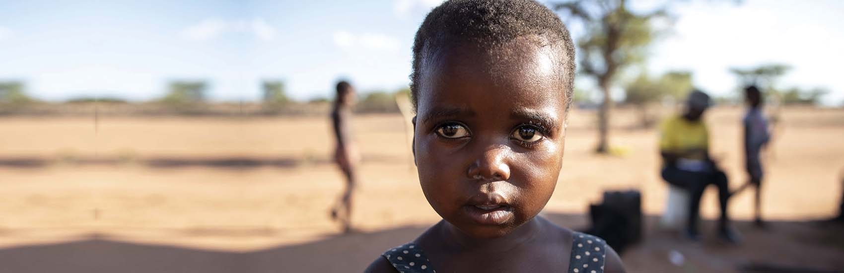 In Zimbabwe, a young girl stand in front of a dry landscape.