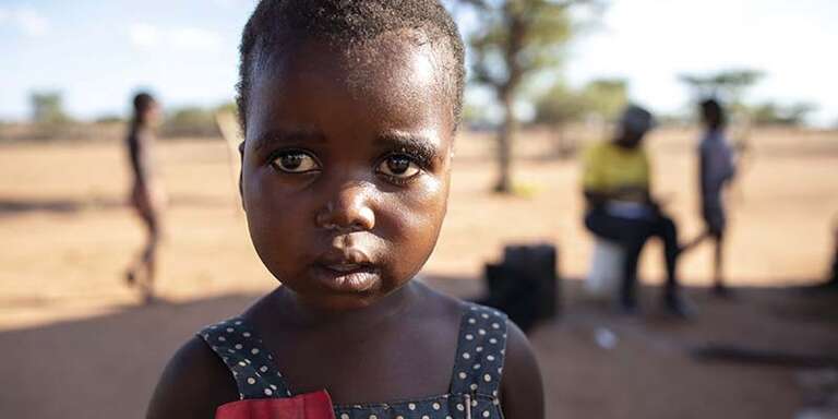 In Zimbabwe, a young girl stands in front of a dry landscape that has been impacted by the climate crisis.