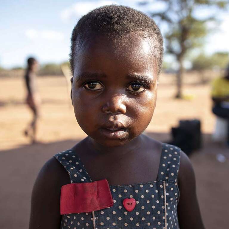 In Zimbabwe, a young girl stands in front of a dry landscape that has been impacted by the climate crisis.