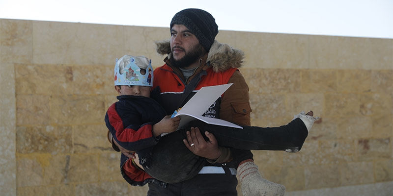 After the devastating earthquakes in Syria, a local aid worker carries an injured young boy