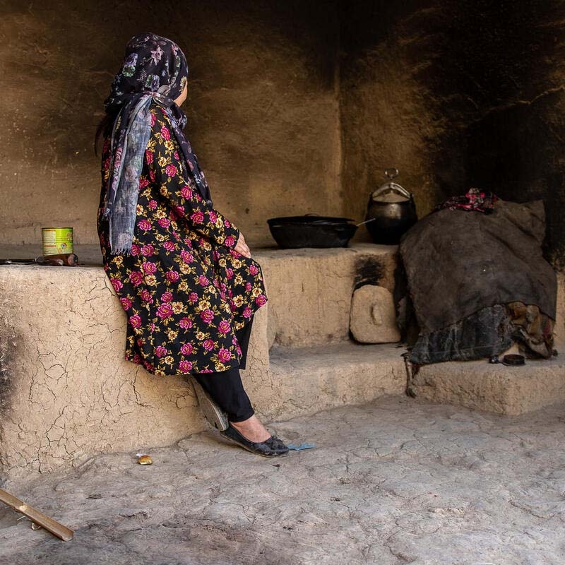 In Afghanistan, a 15-year old girl sits solemnly in her home, where cooking utensils can be seen hanging in the background. 