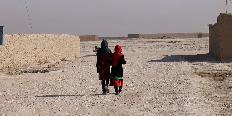 Two girls walk down a dirt road in Afghanistan.