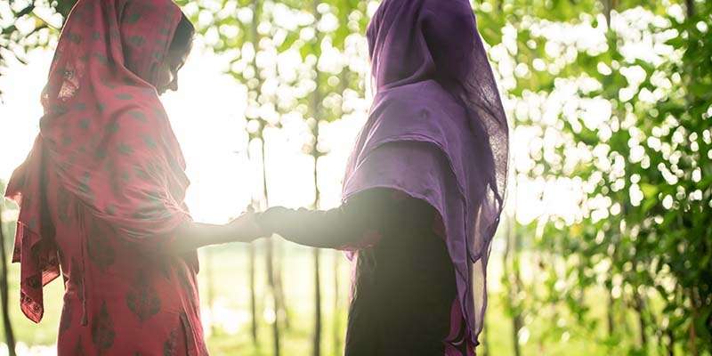 In Bangladesh, two girls laugh and smile while holding hands against the sunrise. 
