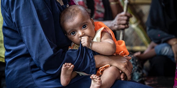 A Rohingya mother sits holding her baby as they wait to be seen by medical staff at Save the Children’s primary health care centre, in a camp for refugees in Cox’s Bazar, Bangladesh.