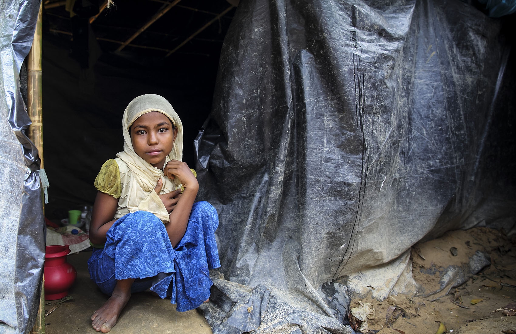Rohingya, a little girl in a yellow top and blue skirt sits in her tent