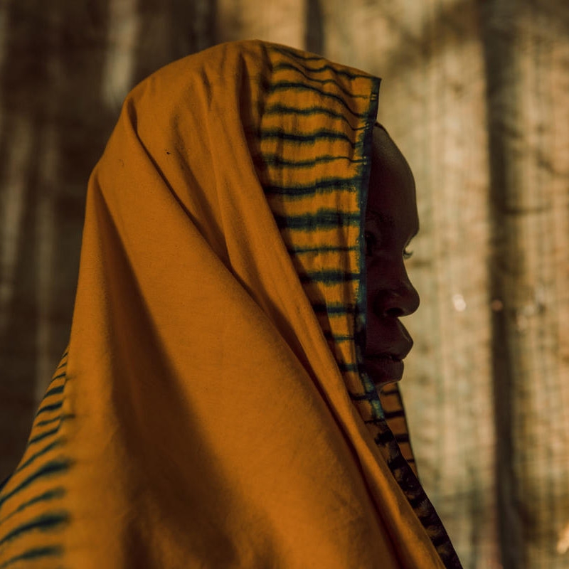 In the Democratic Republic of Congo, a girl wears a covering over her head and turns her head from the camera. 