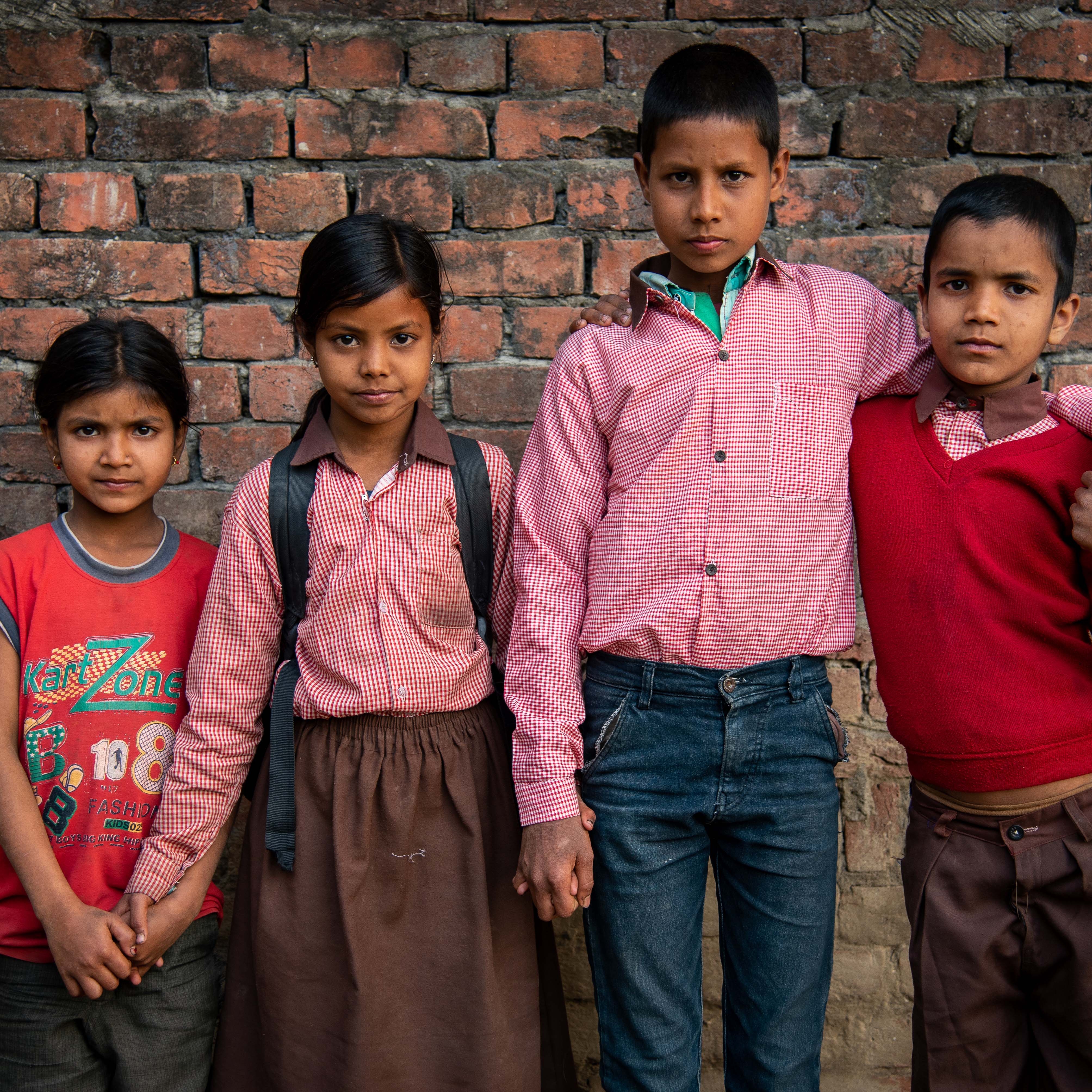A group of four children stand together against a brick wall in India.