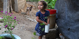 Little girl looking away from the camera, smiling with a baby goat in the background.