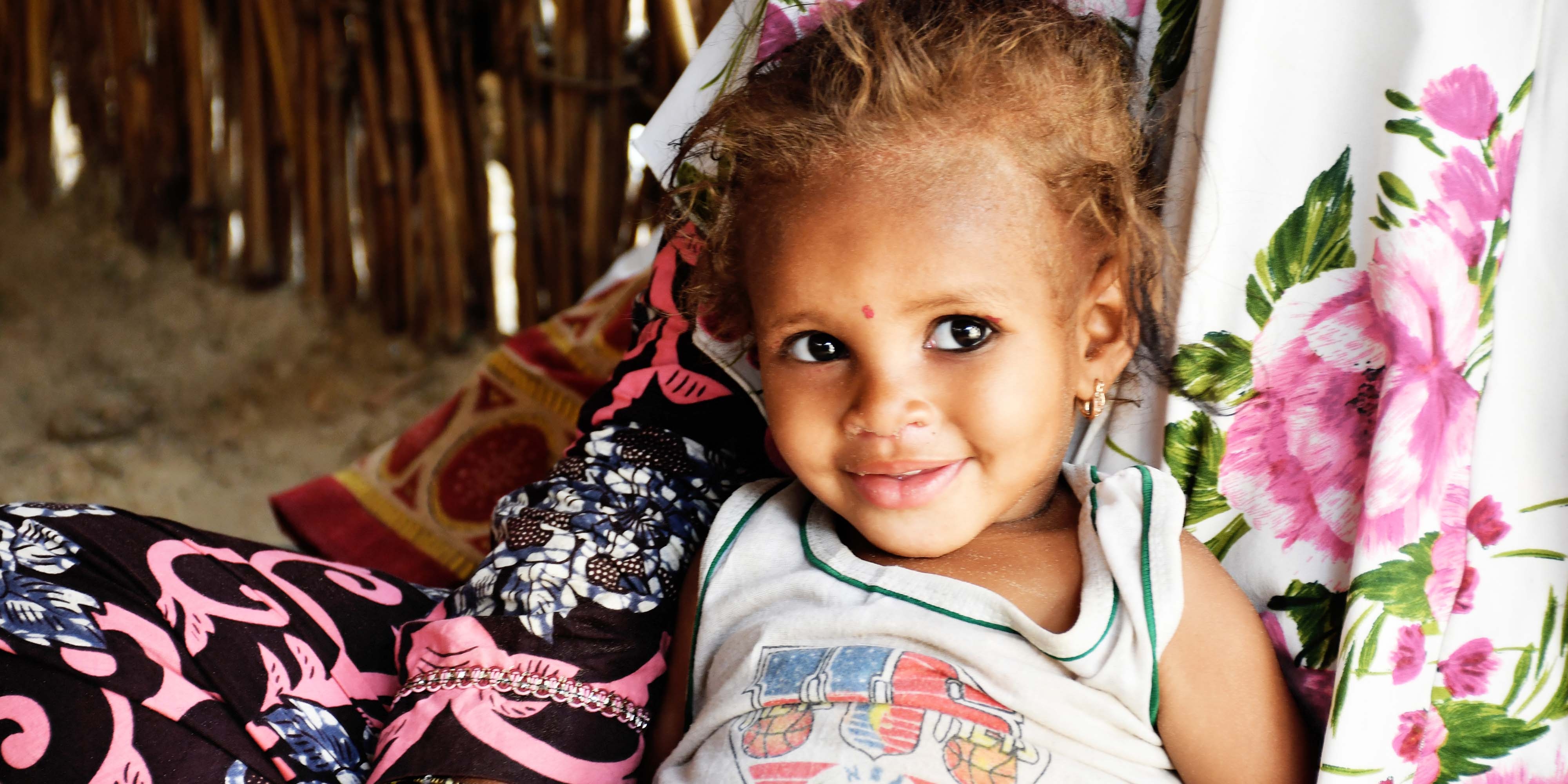 A two-year old girl smiles while resting against her caretaker in Niger. 