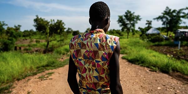 A 14-year old boy and former child soldier from South Sudan, who now lives in a refugee camp in Uganda, walks down a dirt road in a colorful shirt. 