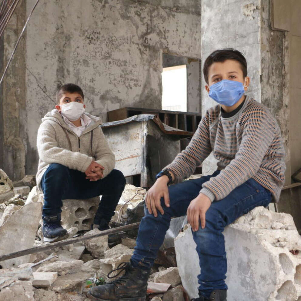 In Syria, two boys sit on rubble from a building destroyed by conflict. 