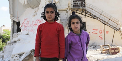 Syria, two little girls stand outside of a destroyed building.
