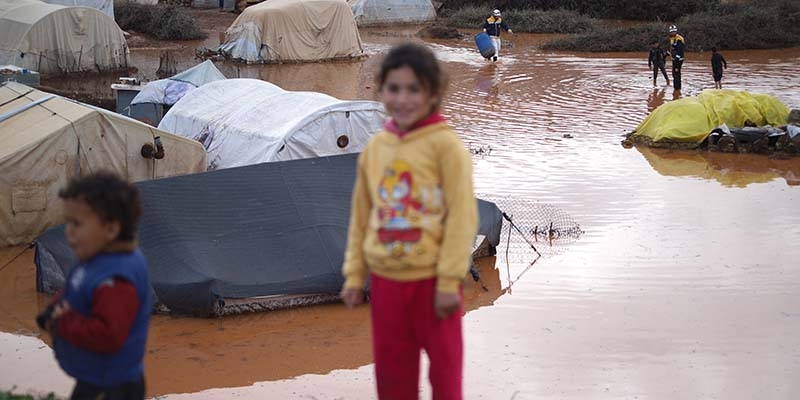Syria, children walk through mud and flood water in a displacement camp in Idlib, Syria. 