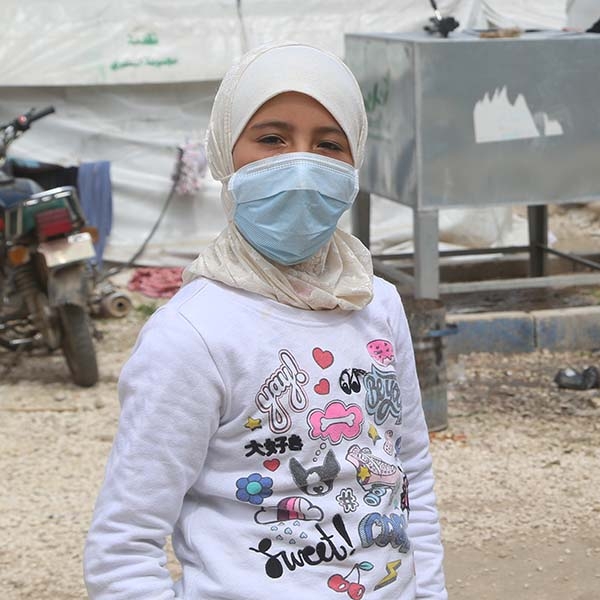 Syria, a refugee girl in a t-shirt and face mask looks at the camera