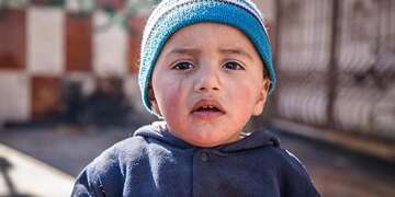 A young Syrian refugee child is photographed standing outside alone. 