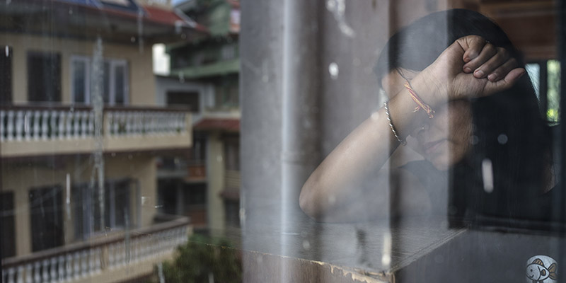 A girl who experienced child trafficking stands with her face covered in front of a window. 