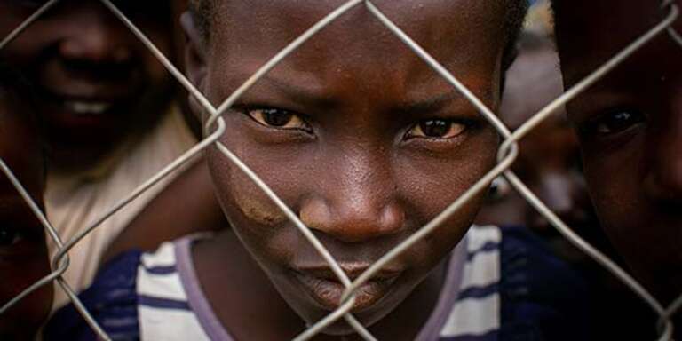 A young Congolese refugee presses his face against a chain link fence in the Kyangwali Refugee Settlement in Uganda.