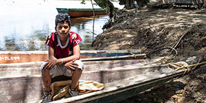 A boy in a red shirt sits in a wooden canoe.