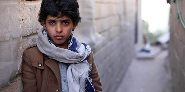 A young boy stands alone near a brick wall in Yemen, where his family's home was hit in an airstrike.