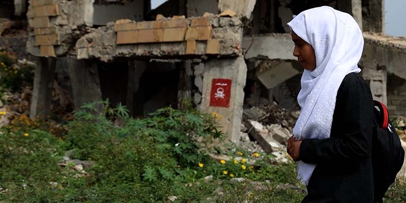 Yemen, a young girl passes a “Danger! Landmines” sign on her damaged school that's contaminated with landmines in Taiz, Yemen. 
