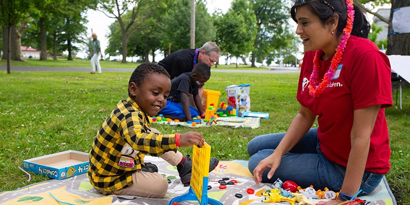 A Save the Children worker sits and plays Connect Four with a small child in a black and yellow shirt.