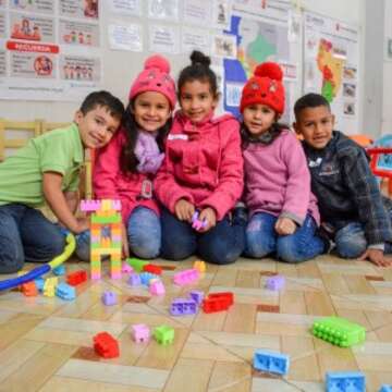 Five children pose for the camera with funny expressions with building blocks in the child-friendly space that Save the Children installs during the delivery of economic assistance to vulnerable Venezuelan families in Lima.