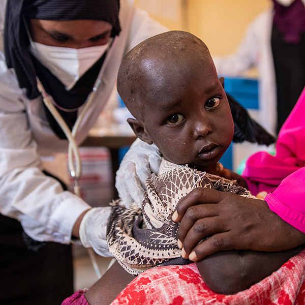 A young child being treated by a doctor sits in her mothers arms. 