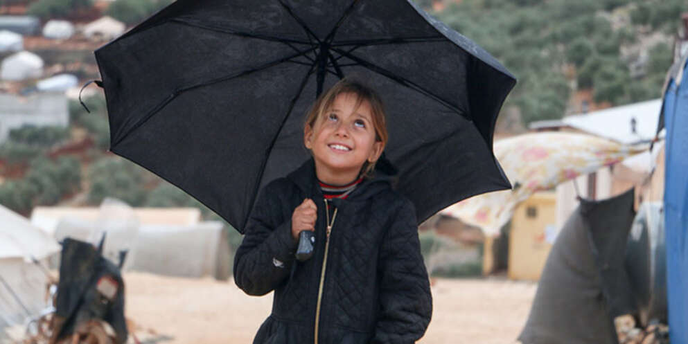 A girl from Syria stands under an umbrella