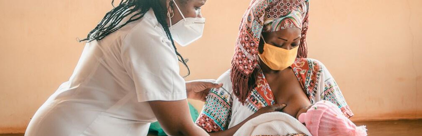 A health care worker in Tanzania helps a mother who is breastfeeding a baby who is laying in her lap. 