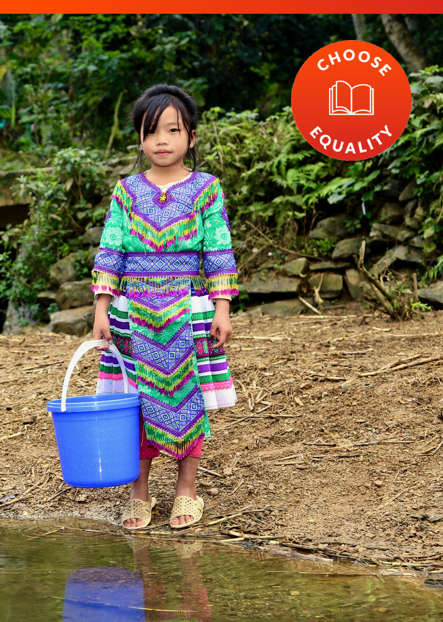 Choose Equality - Child in a colorful dress stands near water with a bucket