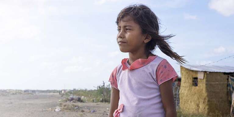In Cambodia, a girl looks out to the horizon while standing on a beach.