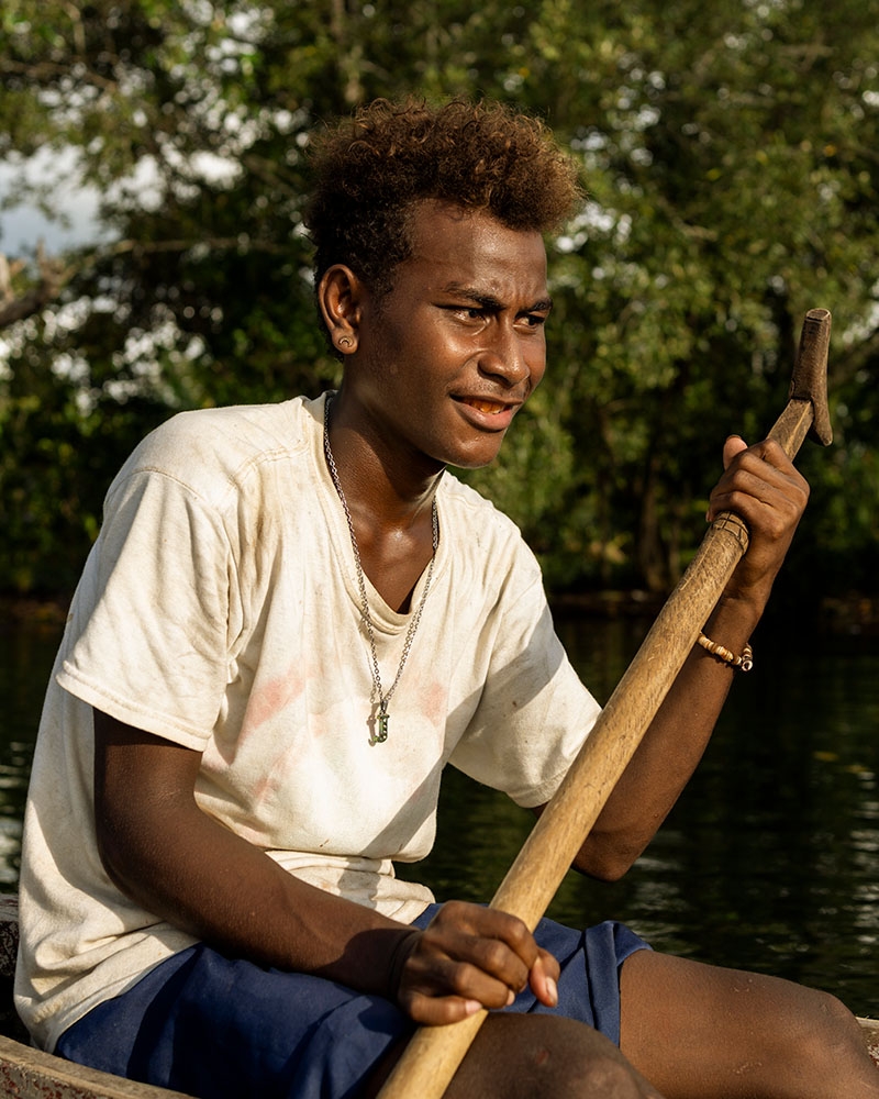 A teenage boy who lives in the Solomon Islands paddles a boat on the water.