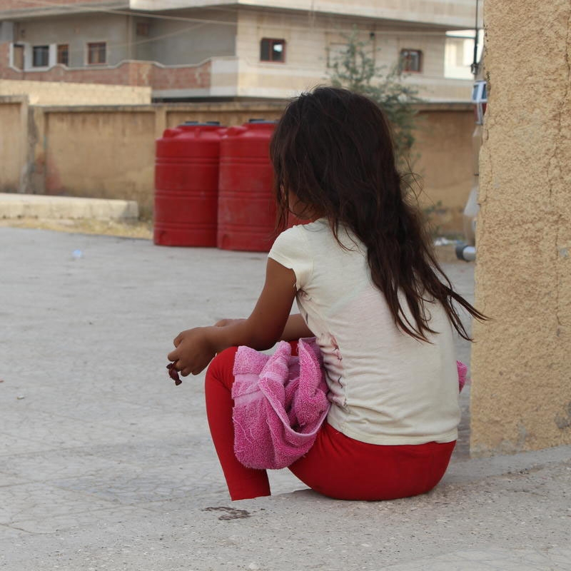 A young girl sits outside her shelter. More than 13,000 people – including approximately 5,200 children – are currently seeking refuge in more than 30 collective shelters. These shelters are schools and unfinished buildings without electricity, as well as open fields across Al Hasakeh, Tal Tamer and Al Raqqa. Photo credit: Save the Children 2019.