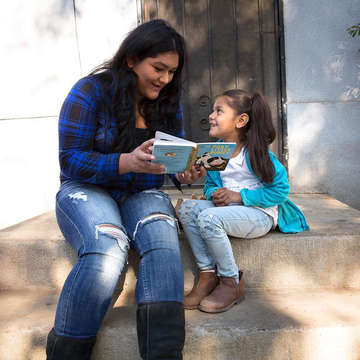 A mother reads a book to her child outside 