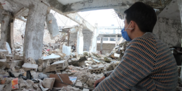A ten-year old boy looks out over the damage done to his by an airstrike school in Syria.