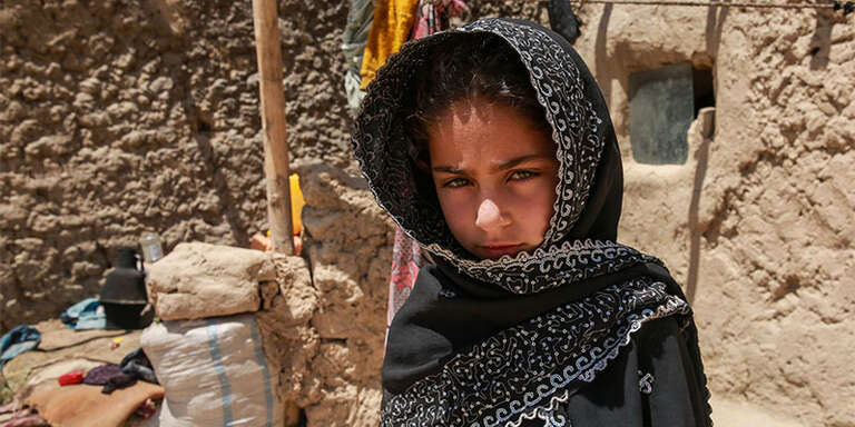 In Afghanistan, a girl smiles while kneeling in her home in a displacement camp for those who have fled conflict.