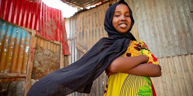 In Somalia, a girl stands confidently with her arms crossed and smiles. 