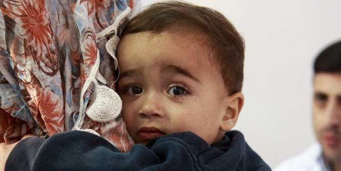 Syria, a toddler looks over a caregiver's shoulder