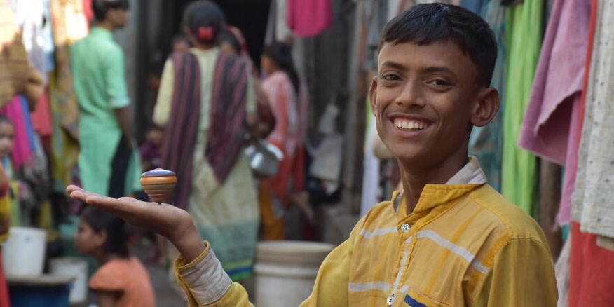 A Bangladeshi boy plays with a toy in a busy alleyway.