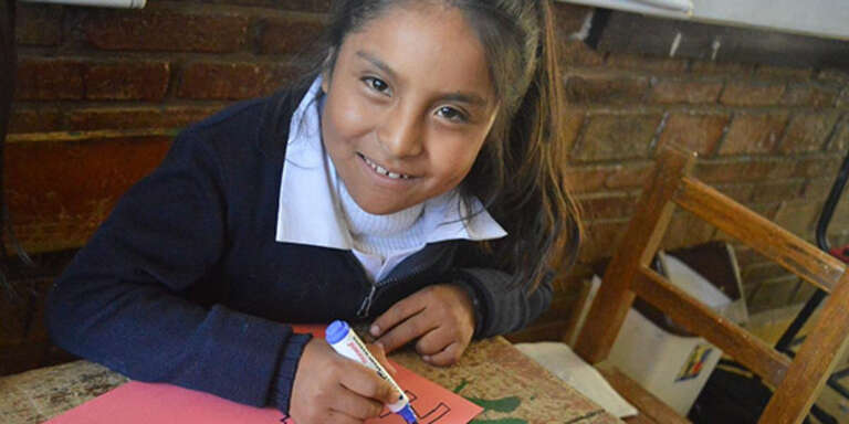 A smiling girl writes during a sponsorship letter writing event in Bolivia.