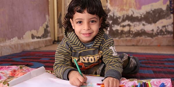 A young child in Egypt, where Save the Children has child sponsorship programs, plays with colored pencils and paper.
