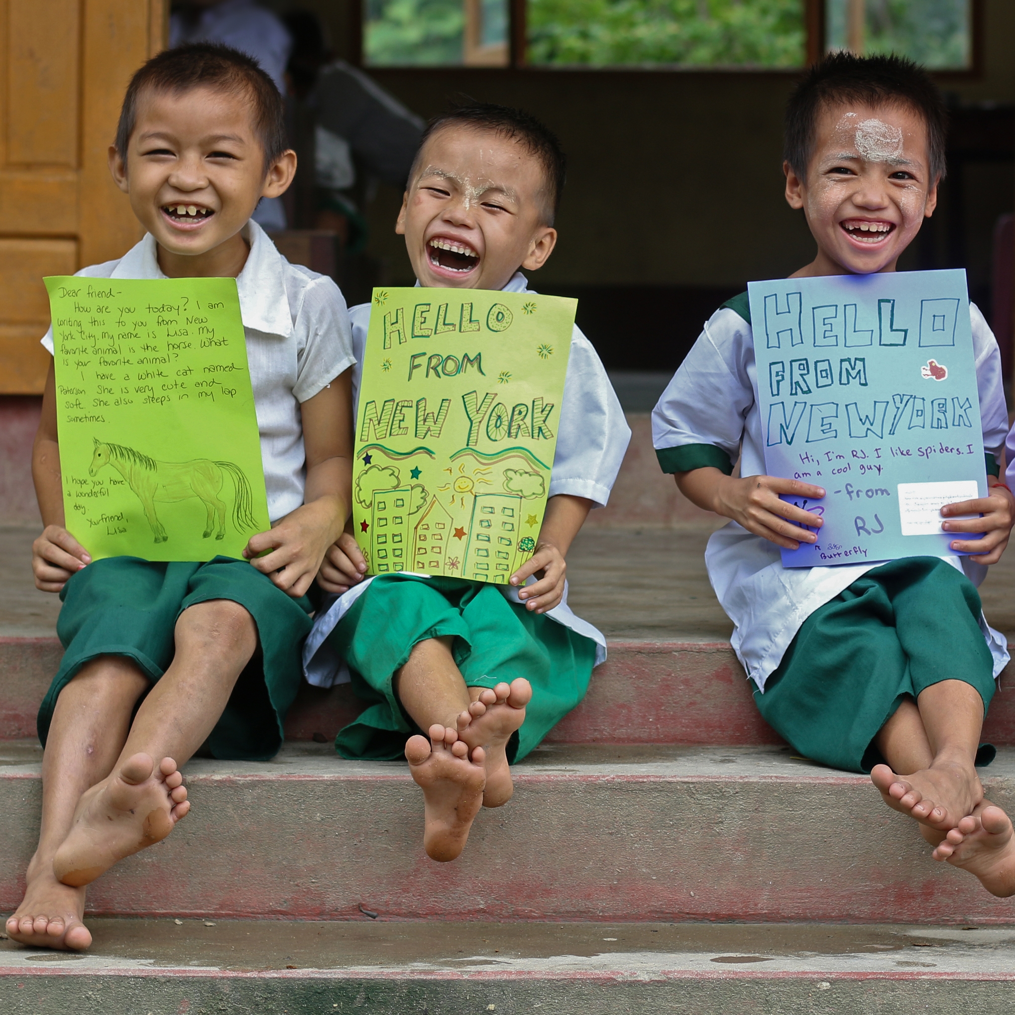 Three young boys in Myanmar smile and hold letters. 